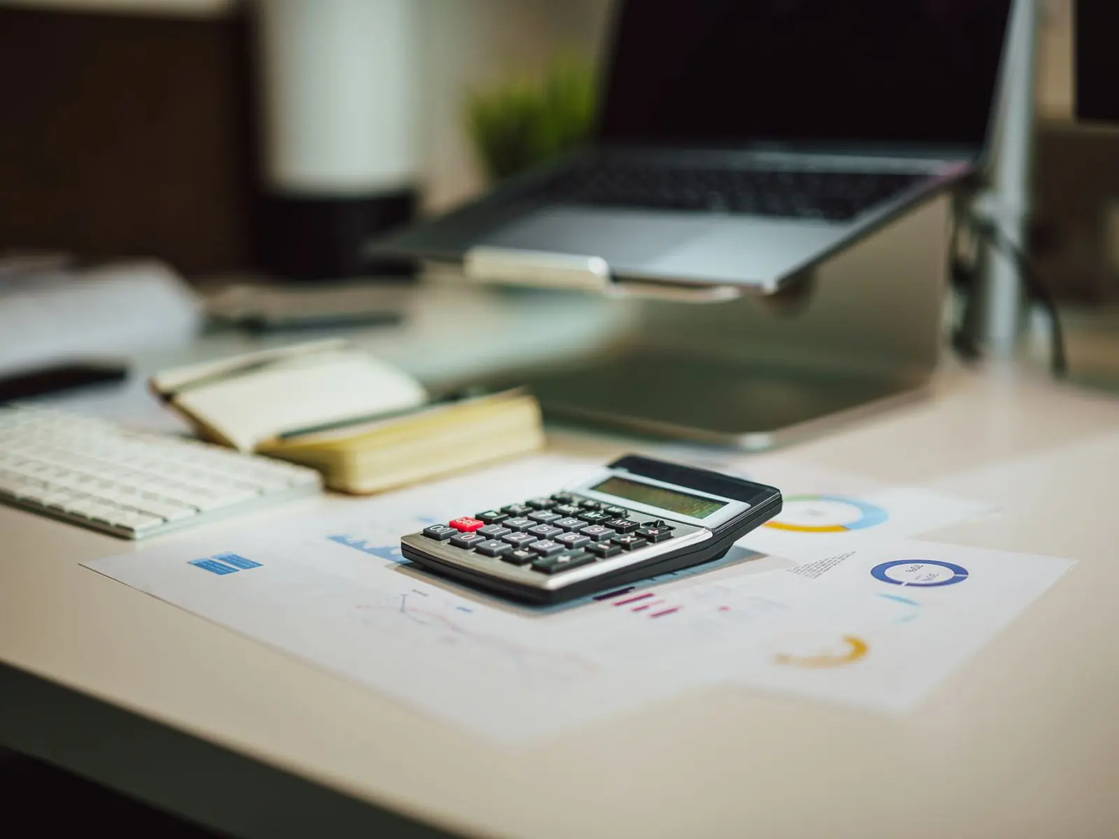 Mesa de una asesoría con un ordenador portátil, una calculadora y gráficos impresos, con luz cálida