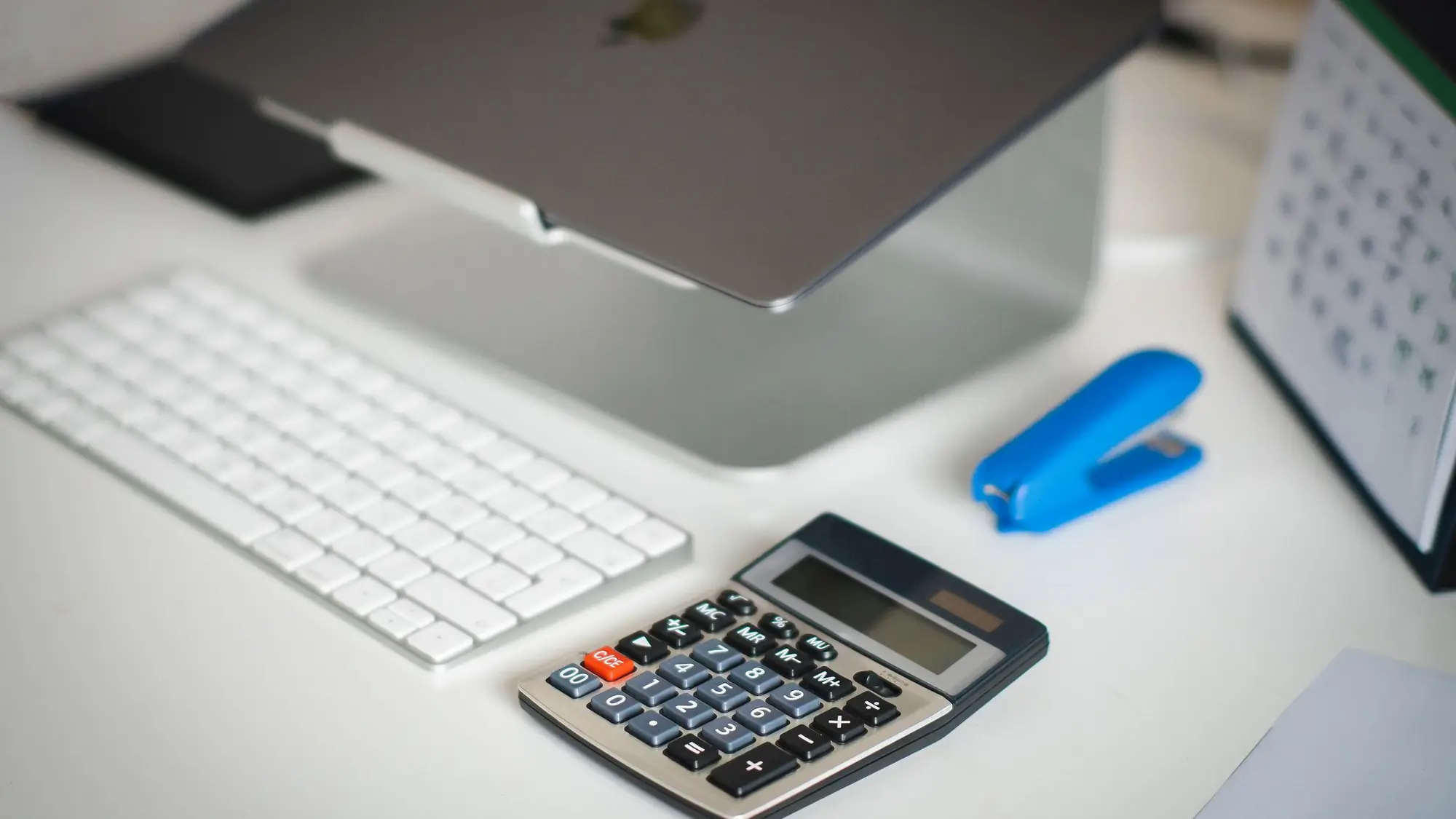 Mesa de oficina ordenada con teclado, calculadora, grapadora y calendario